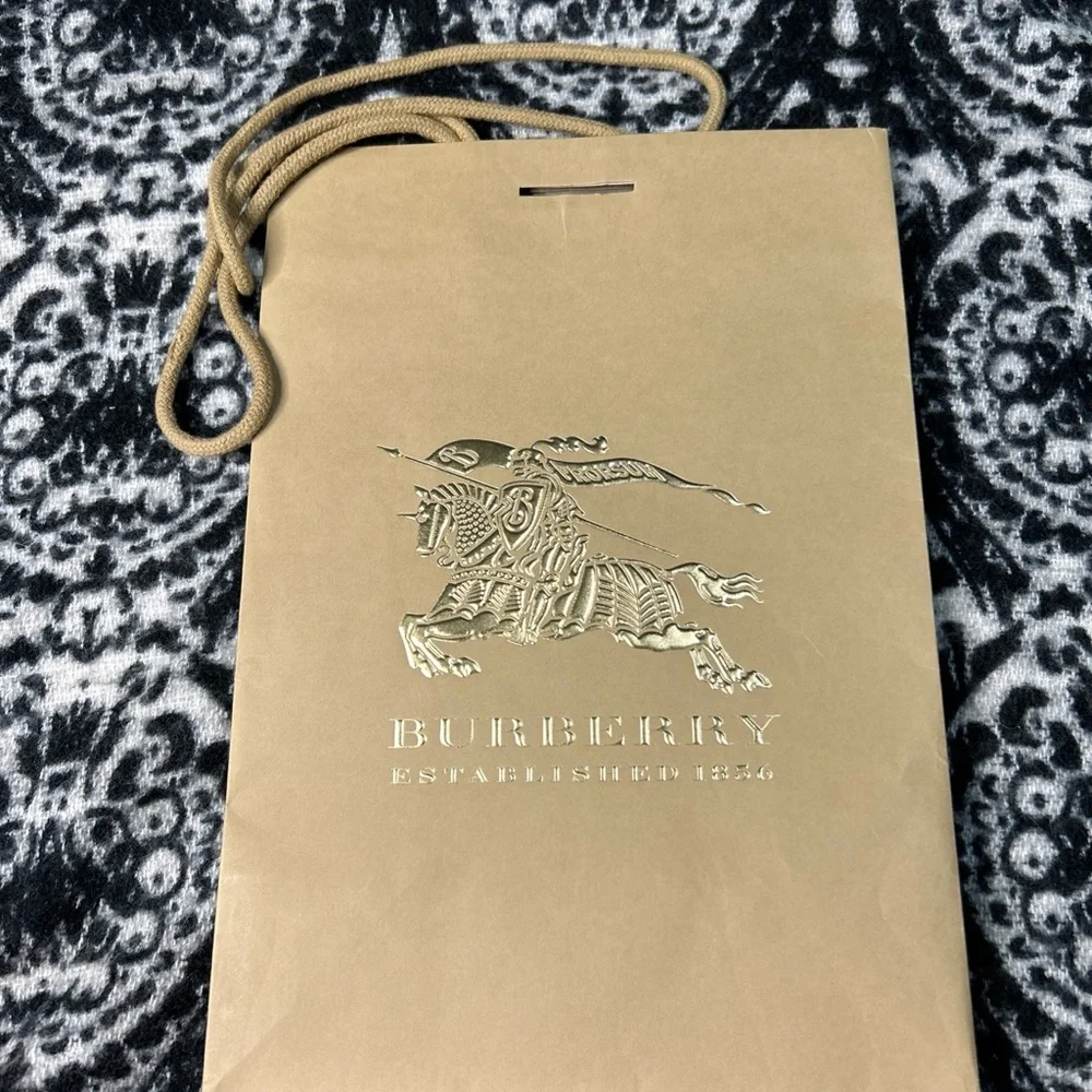 Burberry paper shopping bag with a gold logo and cloth handles.